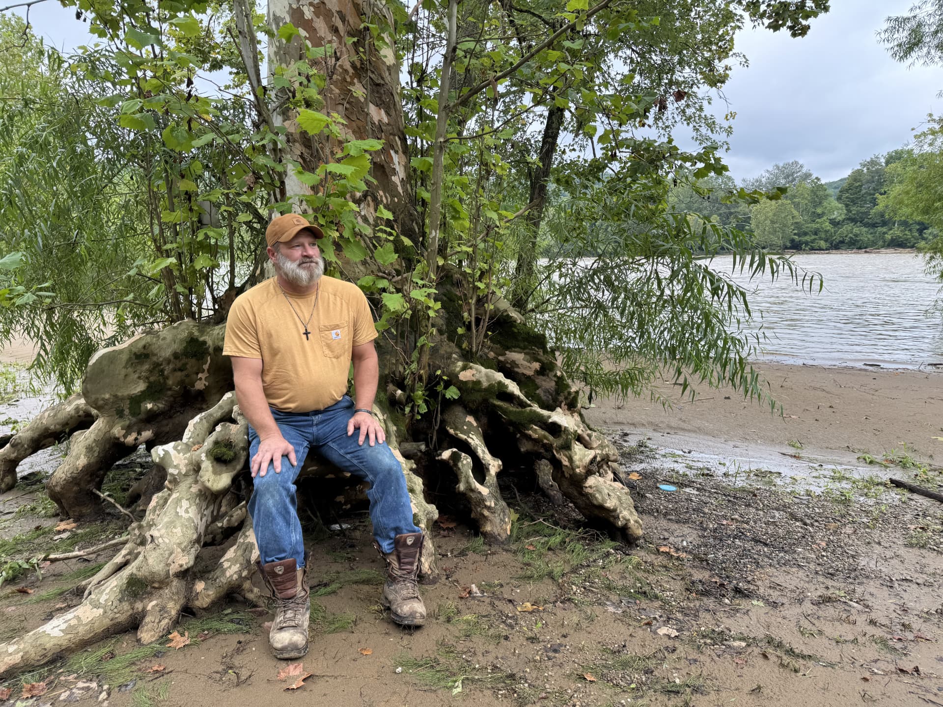 Actor Mike Grigg as Chris Wilson seated on sycamore roots along the riverbank
